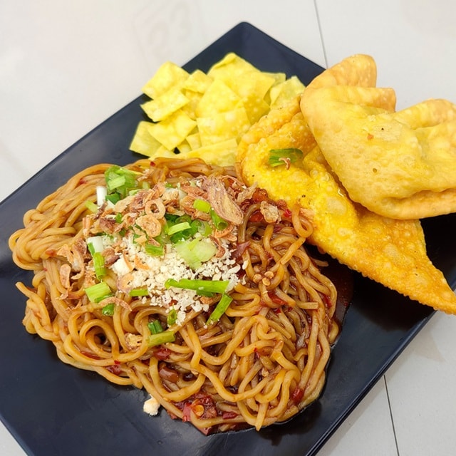 Fried noodles with spicy levels and fried chicken dumplings on a black plate on a white table.  Negative space. Mie goreng dan pangsit goreng. 