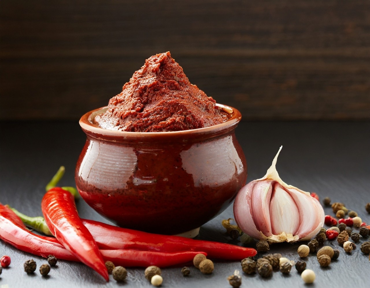 Cabai merah giling dalam wadah tanah liat dengan bahan segar di sekelilingnya.  