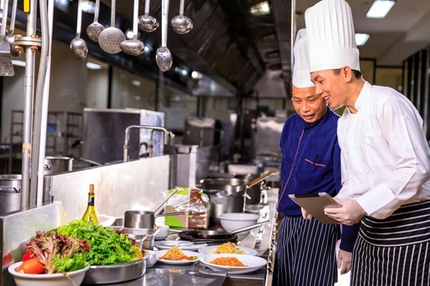 Seperti yang terlihat pada gambar, dua chef sedang berdiskusi di dapur