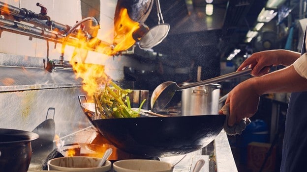 Seperti yang terlihat pada gambar, chef sedang memasak menggunakan wok