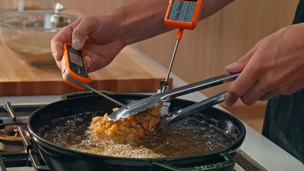 Tangan chef sedang menggoreng ayam dan mengukur tingkat kematangan lewat suhu