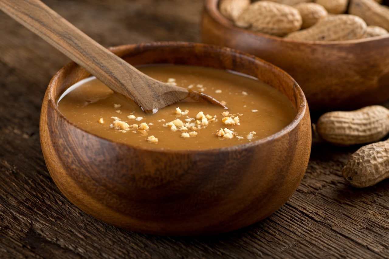 Saus kacang kental dalam mangkuk kayu dengan kacang utuh. 