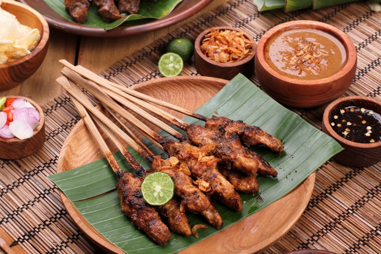 Sate ayam dikelilingi bumbu kacang dan pelengkap sate.  
