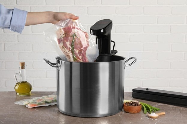 Tangan chef memasukkan daging dalam plastik vakum ke dalam panci berisi alat sous vide. Tangan chef memasukkan daging dalam plastik vakum ke dalam panci berisi alat sous vide.
