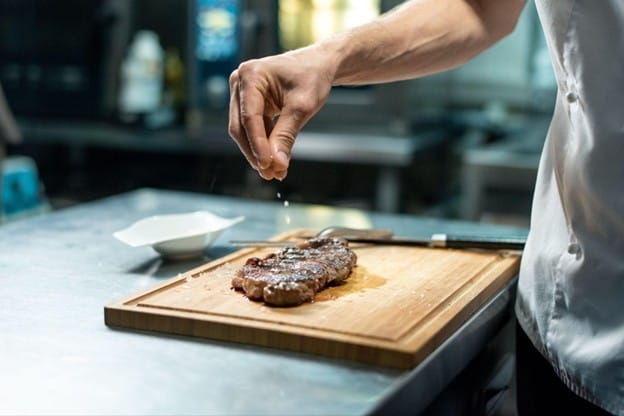 Tangan chef sedang menabur garam ke atas steak daging. Tangan chef sedang menabur garam ke atas steak daging.