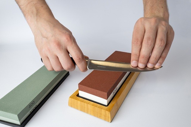 Pisau sedang diasah menggunakan whetstone.  