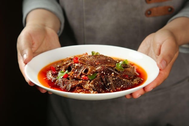 Chef sedang memegang piring berisi tumis babat.