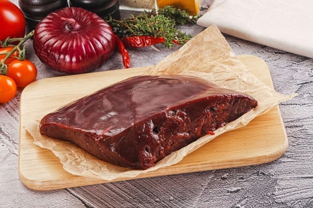 Potongan hati sapi mentah di atas talenan kayu. 