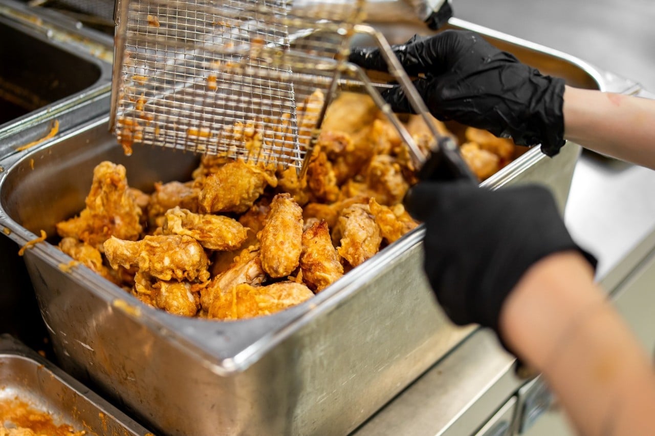 Seperti yang terlihat pada gambar, chef sedang membumbui ayam goreng dalam jumlah banyak