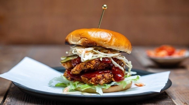Seperti yang terlihat pada foto, ada burger ayam goreng Korea dengan coleslaw, selada, dan saus di atas piring.
