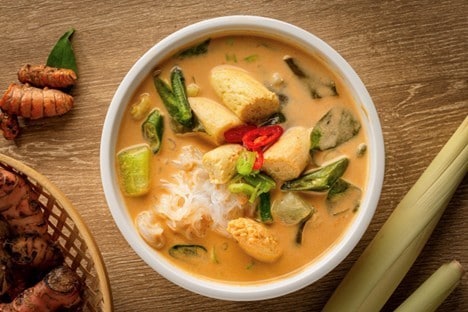  Sayur besan disajikan dalam mangkuk putih dengan bumbu mentah di sekelilingnya. 