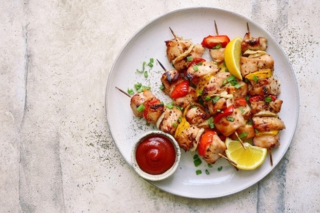 5 tusuk kebab ayam dengan saus tomat di atas piring putih. 5 tusuk kebab ayam dengan saus tomat di atas piring putih.