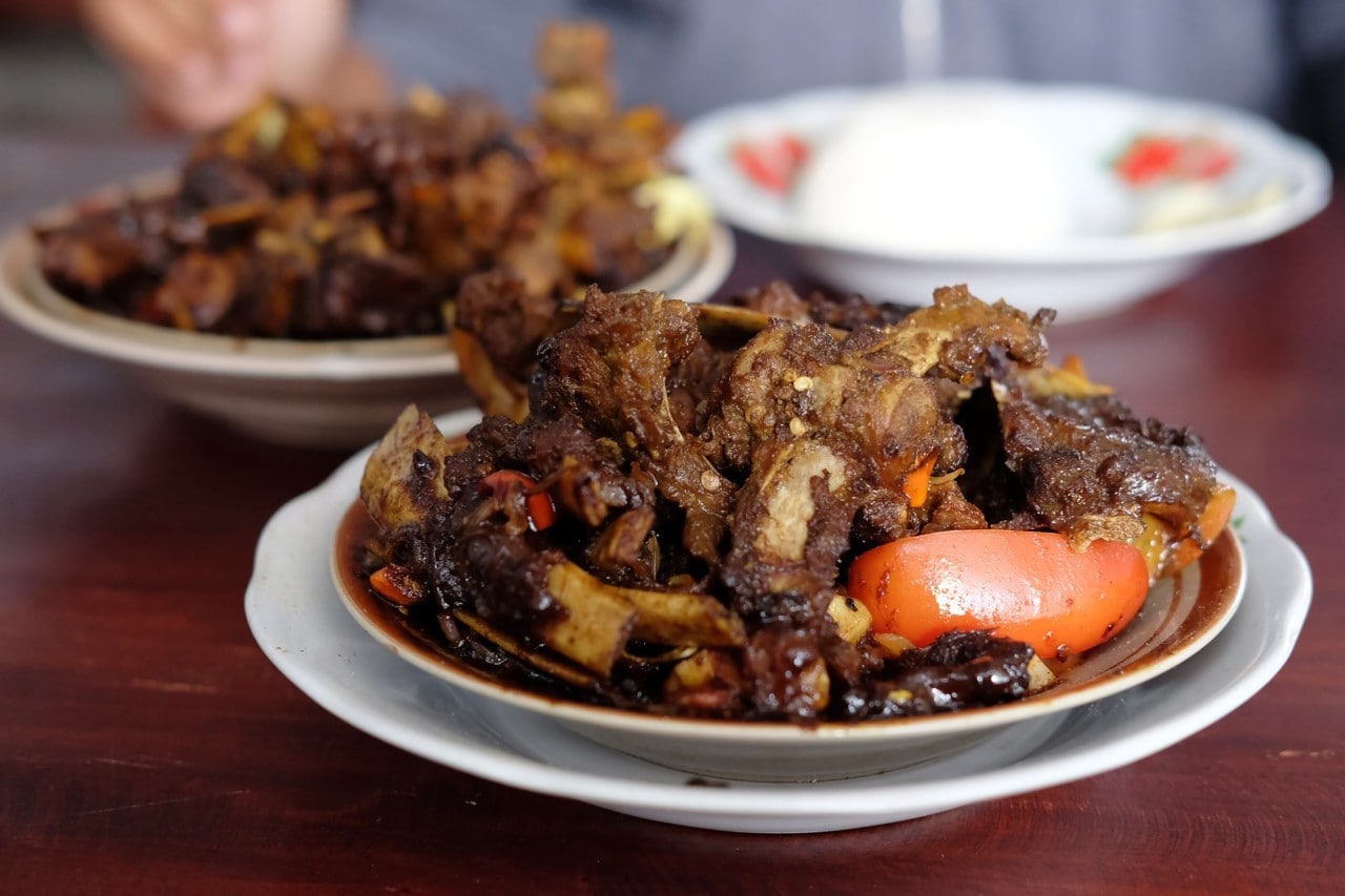 Piring berisi tengkleng kambing dengan potongan tomat.