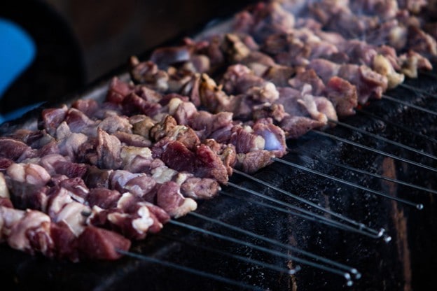 Seperti yang terlihat pada gambar, jejeran sate kambing sedang dimasak di atas bara api