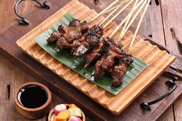 Seperti yang terlihat pada gambar, seporsi sate kambing disajikan di atas wadah saji kayu modern