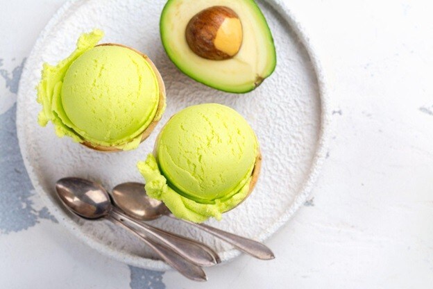 Piring diisi dua scoop avocado ice cream dengan sendok dan avokad segar. Piring diisi dua scoop avocado ice cream dengan sendok dan avokad segar.