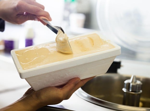 Seperti yang terlihat pada gambar, seseorang sedang menyendokkan es krim ke dalam kemasannya