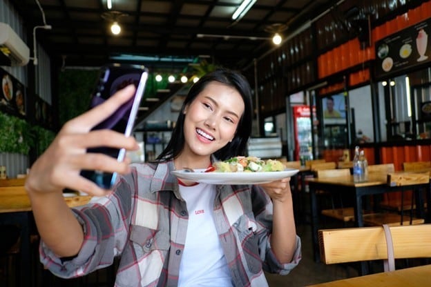 Seperti yang terlihat pada gambar, seorang wanita sedang berswafoto dengan makanan