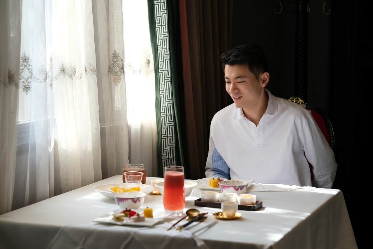 Seperti yang terlihat pada gambar, seorang pria duduk di meja saji sambil tersenyum menatap hidangannya