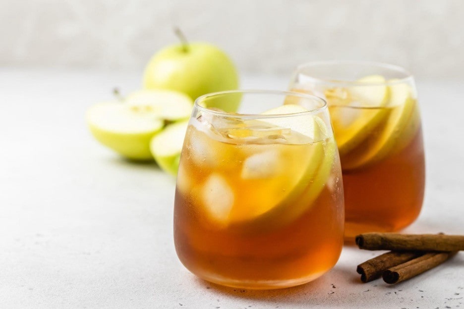 Dua gelas minuman segar diisi apel dengan kayu manis di sampingnya. 
