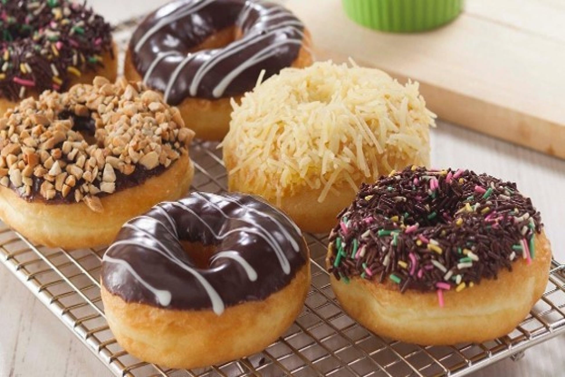 Aneka donat dengan topping cokelat, meses, kacang, dan keju di atas rak kawat.