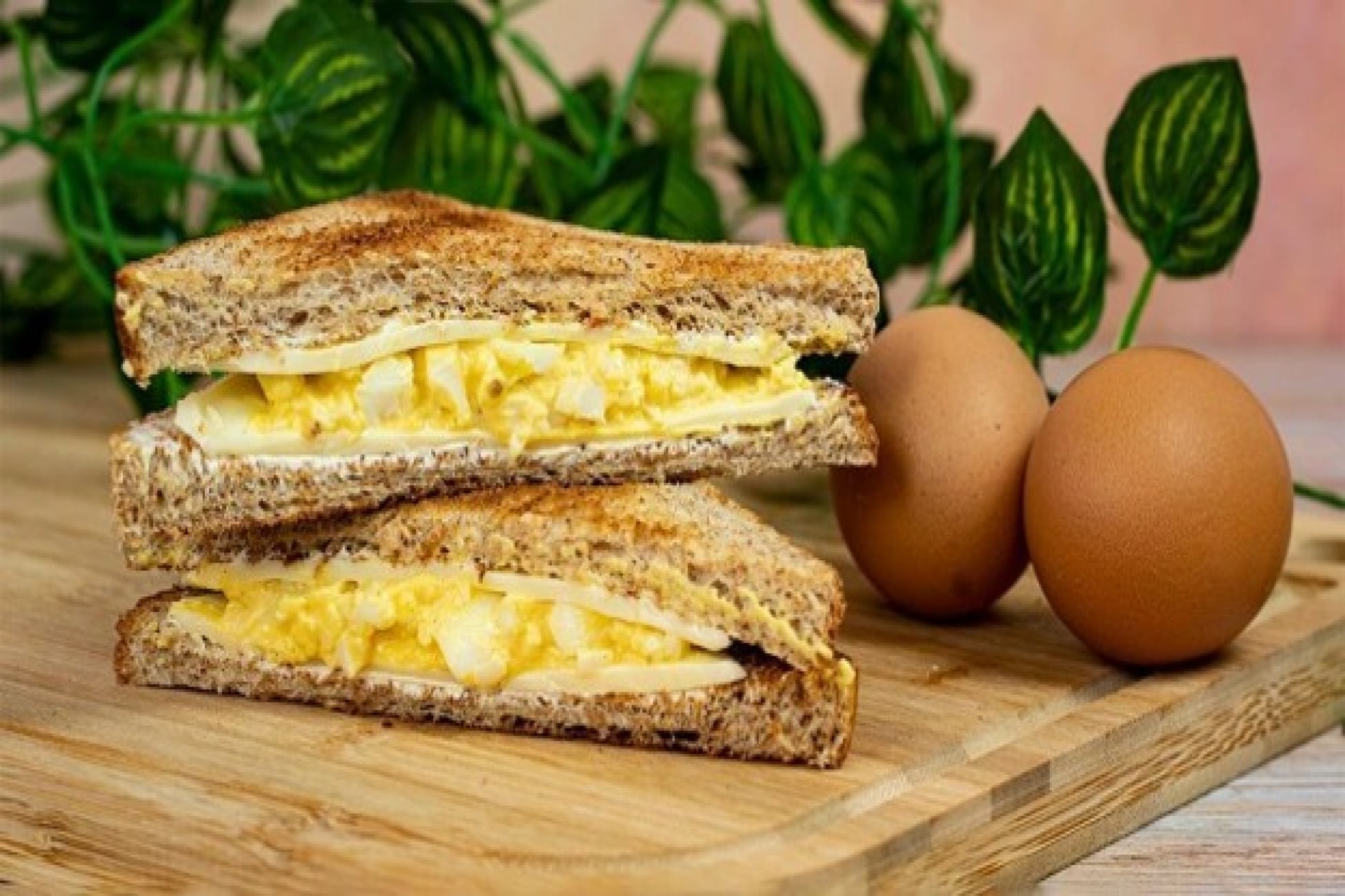 Roti lapis panggang berisi egg mayo disajikan di atas talenan bersama telur rebus.
