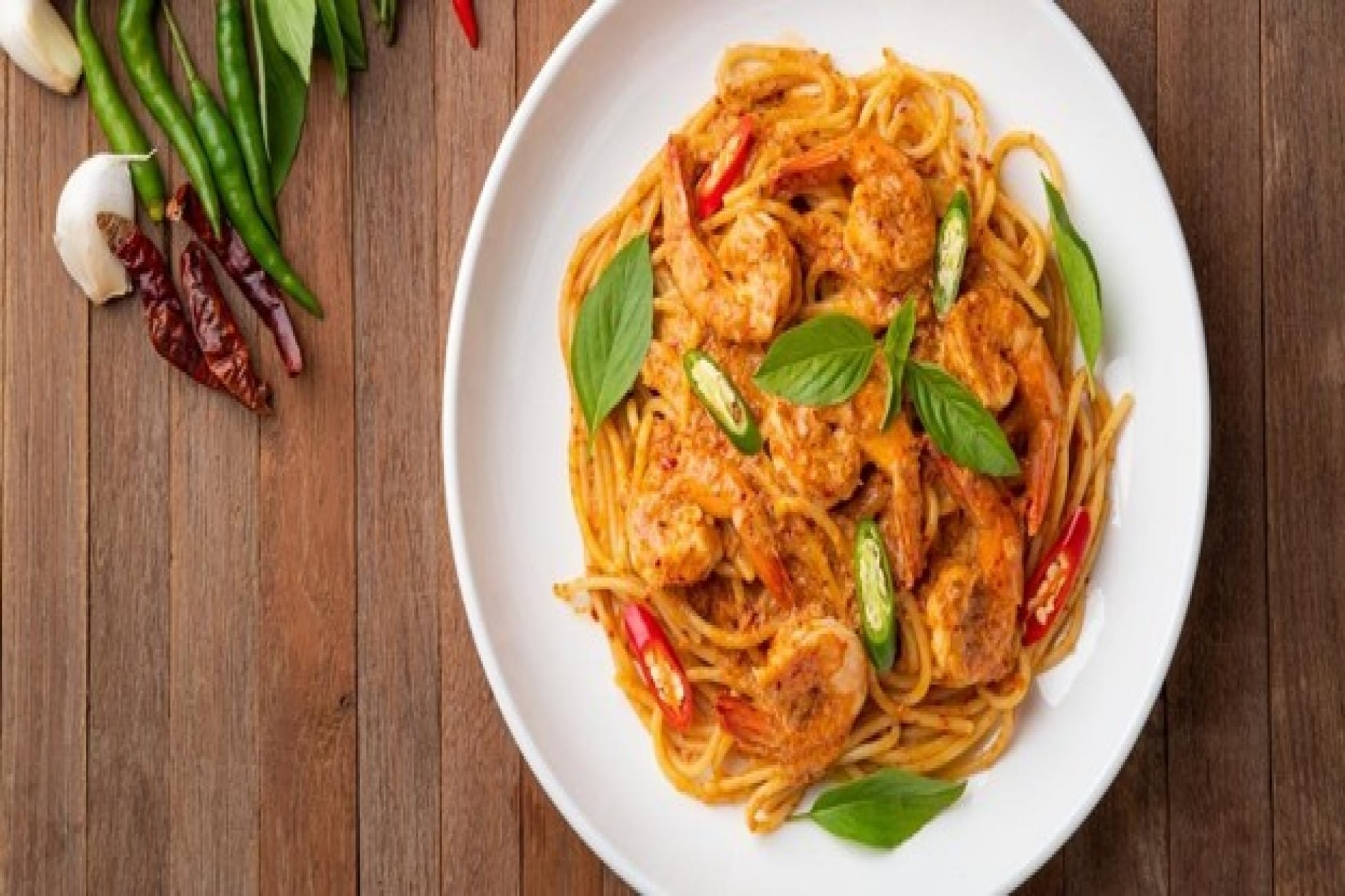 Pasta krim tom yam dengan udang, irisan cabai, dan daun basil.