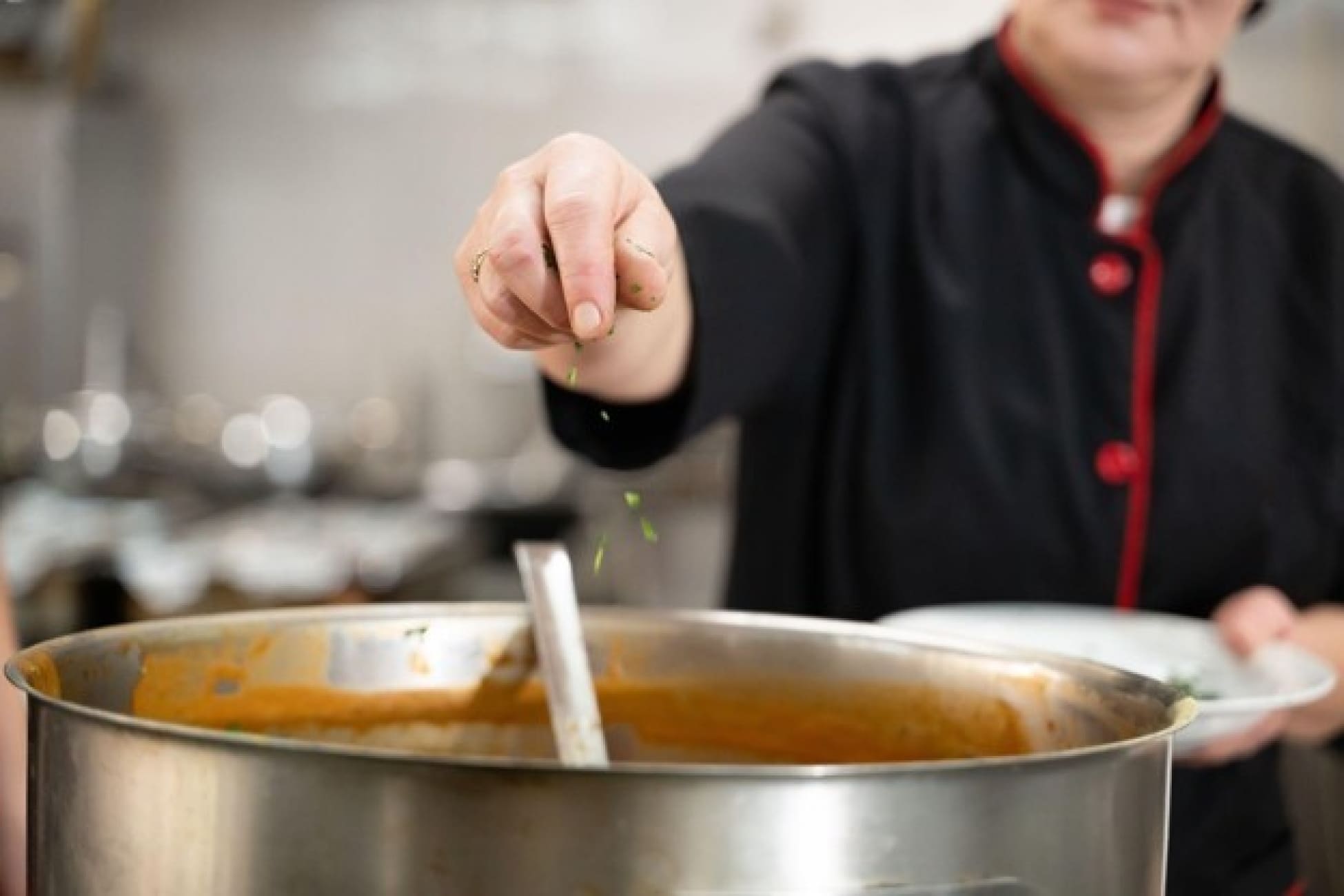 Chef menambahkan bumbu ke dalam satu panci berisi sup di dapur profesional.